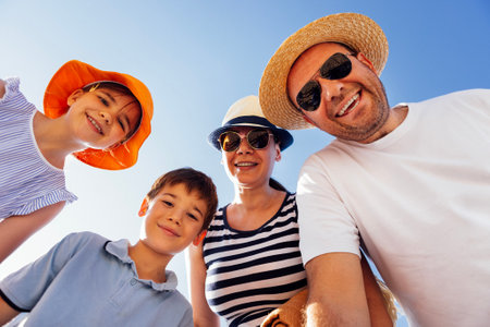 A young happy family on summer vacation at the beach. Cute children and their parents in panama hats smile against the blue sky. A married couple and their children have fun together in natureの写真素材