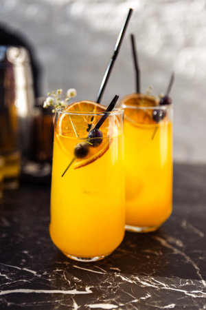 Close-up of two glasses with a citrus cocktail on a black marble table. Tasty chilled drinks are decorated with orange slices, dried flowers and olives. Glasses with straws and delicious juiceの写真素材