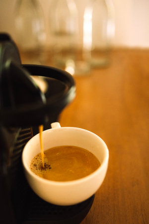 Close-up of a white cup filled with delicious aromatic coffee with milk. The coffee machine stands on a wooden table and makes a tasty coffee drink. The process of making cappuccinoの写真素材