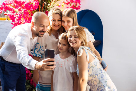 A happy family is photographed at a festive event. A joyful man takes a selfie with his three daughters and his wife. A married couple and their smiling children are looking at the phone screenの写真素材