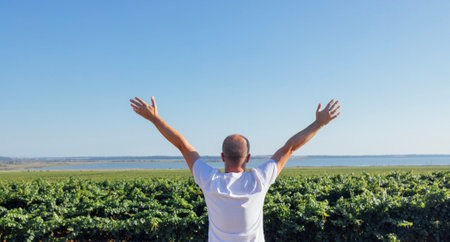 A young man in a white T-shirt spreads his arms and looks at the sea coast. A middle-aged male...