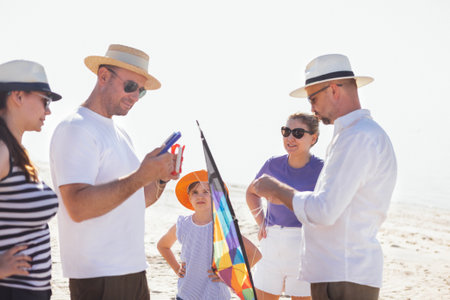 A group of friends are flying a kite on the seashore. Men and women laugh and chat on the beach. A happy family is relaxing and having fun in nature together. Summer holidaysの写真素材