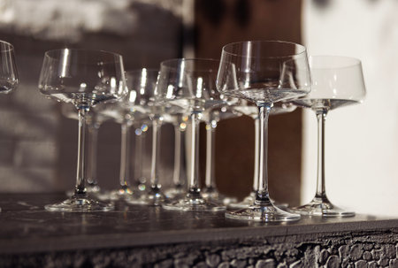 Empty elegant glasses on a long stem on the bar counter. Luxurious goblets on a black marble table. Waiting for the guests at the party. Beautiful bokeh. Copy spaceの写真素材