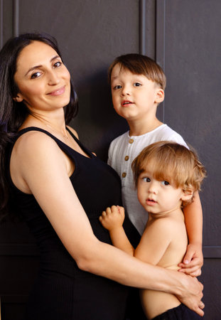 A young pregnant woman hugs her little children at home. Charming mom and her cute sons in casual...