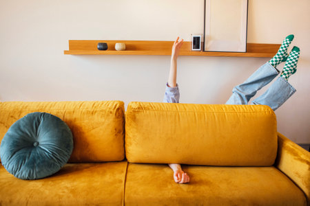 A girl in casual clothes is lying on the couch at home. A woman spread her arms and legs under a pillow on a yellow sofa in the living roomの写真素材