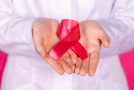 A female hands with a pink satin ribbon with a symbol of the fight against cancer. Cancer Control...