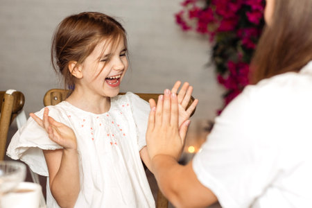 A little girl in a fancy dress is playing with her older sister. The cute child laughs and claps her hands. Happy kid is having fun with her mom outdoorsの写真素材
