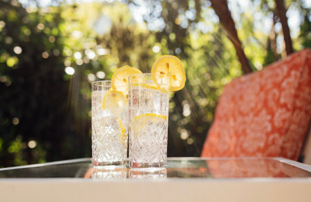 Crystal glasses with delicious cool lemonade on a glass table in the backyard of the house. Elegant cups with citrus carbonated drink. Delicious refreshing summer cocktail with lemon slices outdoorsの写真素材