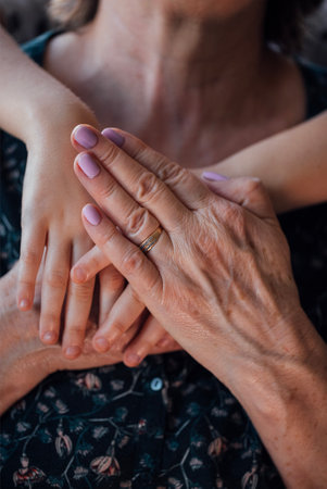 Close-up of a mature woman hands holding the hands of a small child. A kid hugs his grandmother by the shoulders. Hugs of a baby and an elderly ladyの写真素材