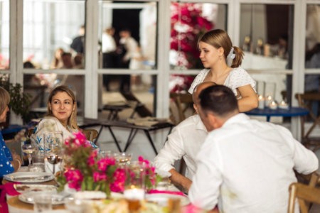 Small talk between women and men of different ages at the festive table. A happy family and their friends are chatting at a celebratory meeting. The stylish interior of the restaurantの写真素材