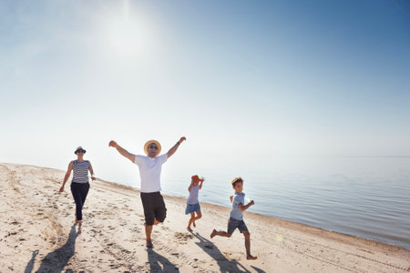 A happy family runs along the seashore. A young man and his kids spread their arms and laugh on a sandy beach. A married couple and a kid relax and have fun in nature during their summer holidaysの写真素材