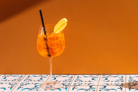 Close-up of a glass with a piece of orange. A cup of cool, delicious sour orange drink with ice cubes. Citrus alcoholic cocktail and straw on a patterned tile table. Copy spaceの写真素材
