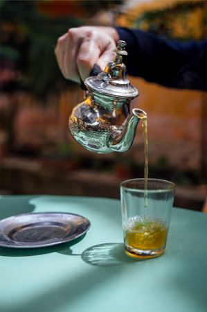 Man pouring mint tea, close up. Silver oriental teapot kettle and tea cup glass to drink traditional...