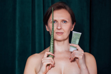 A middle-aged woman holds an aloe leaf and a tube of gel. A young lady with bare shoulders and no makeup smiles and holds a mock-up tube of cream and a sheet. Natural ingredients of cosmetic productsの写真素材