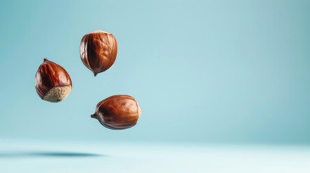 Three chestnuts are suspended in the air against a calming blue backdrop, highlighting their glossy surface and rich brown tones, creating an inviting atmosphere, AI generatedの素材