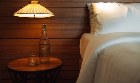Inviting bedroom setup with a wooden nightstand, glass of water, and bottle, softly lit by a warm...