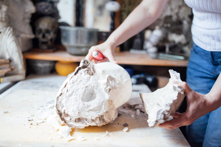 Artist is shaping a plaster skull in a creative workspace, with various tools and artistic elements...