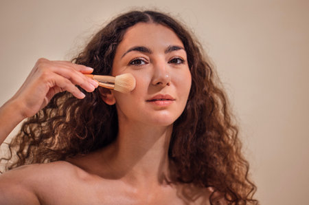 Female makeup applying with a brush, highlighting beauty routine and self-care, surrounded by soft...