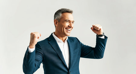 Middle-aged man in a blue suit is joyfully celebrating success with raised fists, surrounded by a bright and minimalistic backdrop, conveying a sense of achievement and positivity, AI generatedの素材