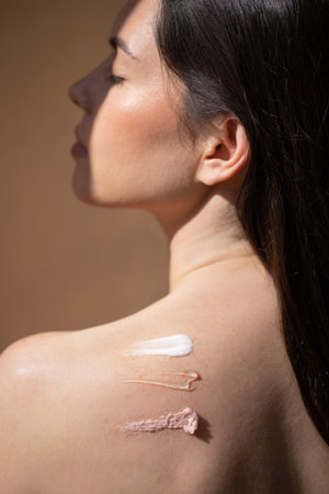Female model with long dark hair displays skincare products on her shoulder, emphasizing various textures and colors, creating a serene beauty atmosphereの写真素材