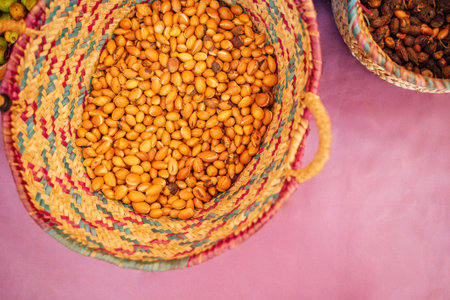 Woven basket brimming with golden argan nuts rests on a purple surface, highlighting rich textures and colors, ideal for food-related projects and organic themesの写真素材