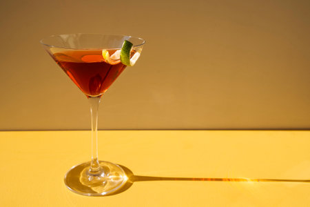 Close-up of a martini glass on a yellow background. An elegant goblet with a red alcoholic sparkling...