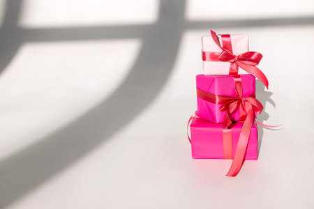 Three gifts in bright packaging and satin bows on a white background. Present boxes in different colors with pink ribbons. Copy spaceの写真素材