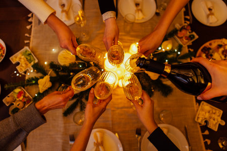 Diverse hands raise champagne glasses in a toast around a beautifully set table, filled with delicious food and festive decorations, creating a joyful atmosphereの写真素材