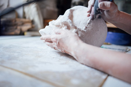 Artisan is meticulously sculpting a clay head in a creative workspace, surrounded by tools and materials, highlighting the artistry and dedication involved in the craftの写真素材