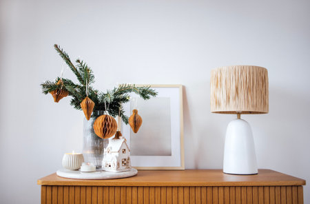 A beautifully styled tabletop showcases a modern lamp, a festive arrangement of greenery, and a quaint miniature house, enhancing the warm ambiance of the spaceの写真素材