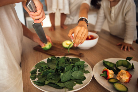 Woman prepares fresh vegetables on a wooden cutting board, with family members nearby, creating a lively cooking atmosphere filled with healthy ingredients and culinary joyの写真素材
