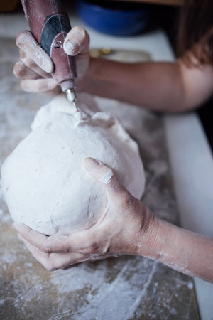 Artisan is meticulously shaping a clay sculpture using a rotary tool, surrounded by various...