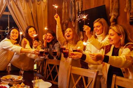 Young women in knitted sweaters laugh and raise glasses of mulled wine. Friends have fun and drink...