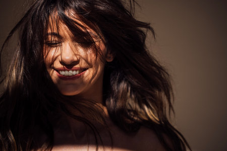 Joyful woman with flowing hair is illuminated by soft light, showcasing a bright smile and natural beauty, creating a serene and uplifting atmosphereの写真素材