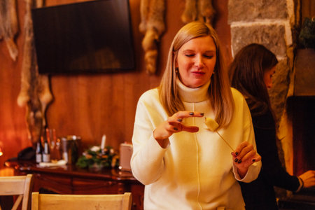 Close-up of a female hands holding a marshmallow toasted on fire. A laughing woman in a sweater eats...