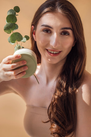 Female model with long brown hair is holding a small potted plant, embodying a connection to nature and promoting an eco-friendly lifestyle in a serene atmosphereの写真素材