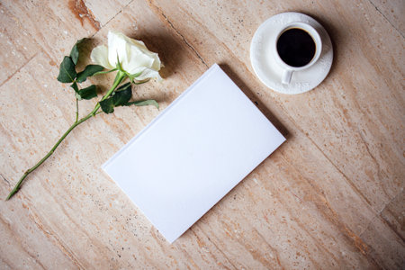 Blank notebook positioned next to a cup of coffee and a white rose on a stone surface, evoking a calm and creative workspace for inspiration and reflectionの写真素材