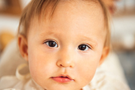 Child with light brown hair looks directly at the camera, surrounded by soft textures and warm colors, evoking feelings of innocence and curiosity in a cozy settingの写真素材