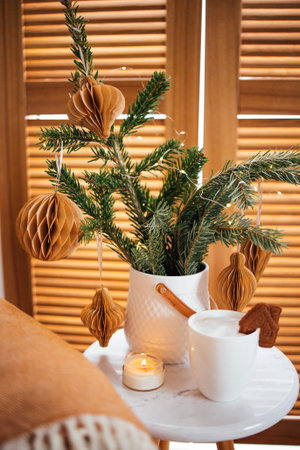 Small evergreen tree decorated with honeycomb ornaments sits on a marble table beside a cozy cup of hot beverage, enhancing the festive ambiance of the spaceの写真素材