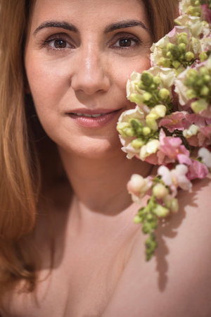 Female subject with long brown hair, surrounded by vibrant flowers, presents a serene expression in a close-up portrait, showcasing natural beauty and eleganceの写真素材