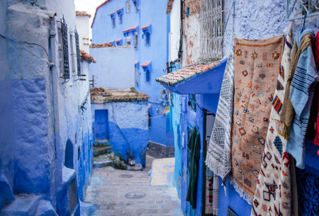 Vibrant blue alleyway in Chefchaouen, Morocco, features traditional textiles hanging from walls, surrounded by unique architecture, creating an inviting atmosphere for exploration and cultural immersionの写真素材