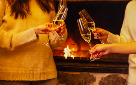 Women are toasting with champagne glasses in front of a warm fireplace, creating a cozy ambiance filled with joy and celebration during a festive occasionの写真素材