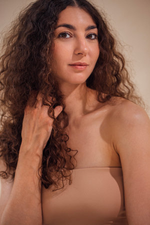 Woman with curly hair poses elegantly against a soft neutral backdrop, highlighting her natural beauty and serene expression in a calm and inviting atmosphereの写真素材