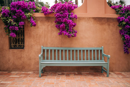 A charming wooden bench positioned against a textured wall, surrounded by lush purple bougainvillea flowers, offering a peaceful outdoor space for relaxation and enjoymentの写真素材