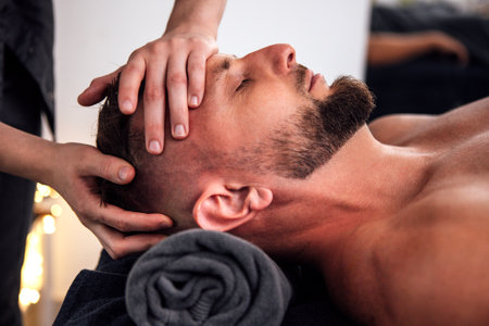 Male individual enjoys a soothing head massage in a tranquil spa setting, surrounded by soft lighting and towels, enhancing relaxation and wellness experienceの写真素材