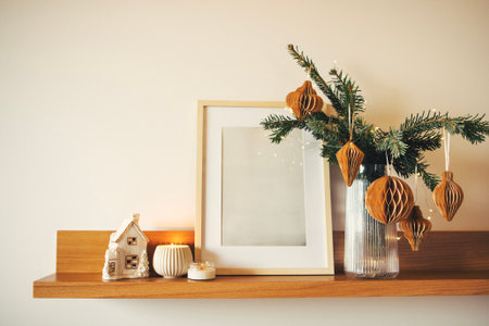 Shelf display includes a blank picture frame, a decorative house ornament, a candle, and festive greenery with paper ornaments, enhancing a warm holiday ambianceの写真素材