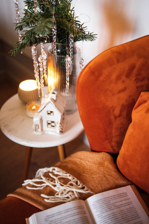 Inviting living room setup with an orange armchair, a decorative plant in a vase, candlelight, and an open book on a side table, perfect for cozy momentsの写真素材