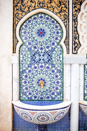 Decorative fountain with detailed tile patterns in blue and green, set against a textured wall,...