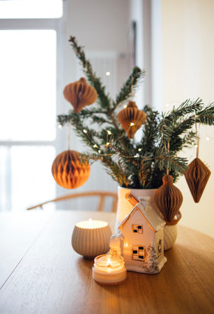 Decorative evergreen tree adorned with ornaments and surrounded by candles and a ceramic house, enhancing the festive ambiance in a warm indoor spaceの写真素材