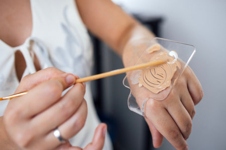 Makeup artist demonstrates foundation application on hand with spatula, highlighting skin tone matching techniques and beauty skills in a well-lit studio settingの写真素材